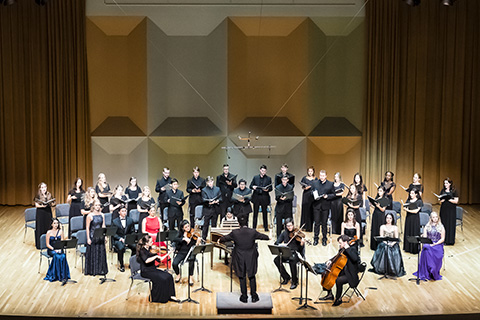 Musicians with string instruments and a choir perform live